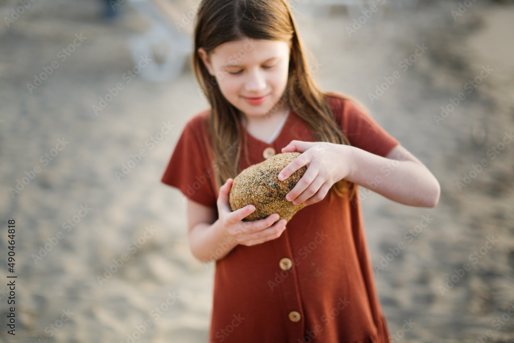 Cute long-haired European baby girl in a dress on the sea coast. Girl and stones at sunset on the ocean. Cute long-haired European baby girl in a dress on the sea coast. Girl and stones at sunset on the ocean.