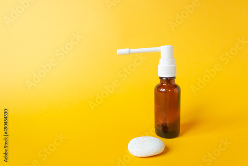 Glass brown spray bottle with white nozzle and white stone isolated on yellow background. For throat infection.