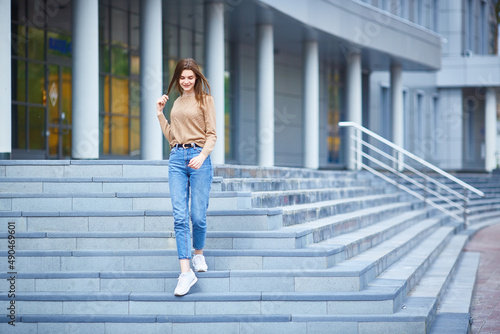 young woman walks down the steps of a gray building on a cold summer day or warm autumn.
