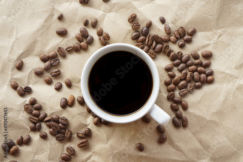 Flat lay view of black coffee cup on crumple brown paper with coffee beans