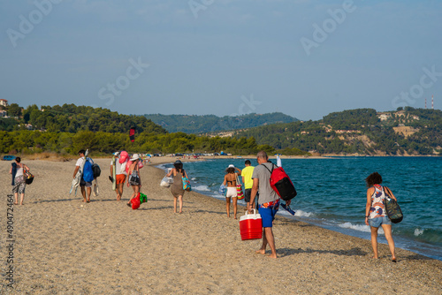 Large Group of excited young friends and people in summer clothes going for a picnic and swimming at the sea beach. Beautiful scenic view of iconic Posidi sandy beach, paradise cape.