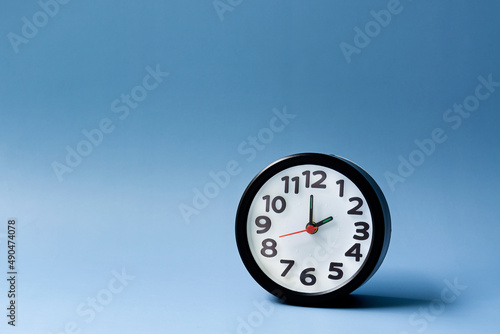 Black alarm clock isolated on blue background. The clock set at 2 o'clock. photo