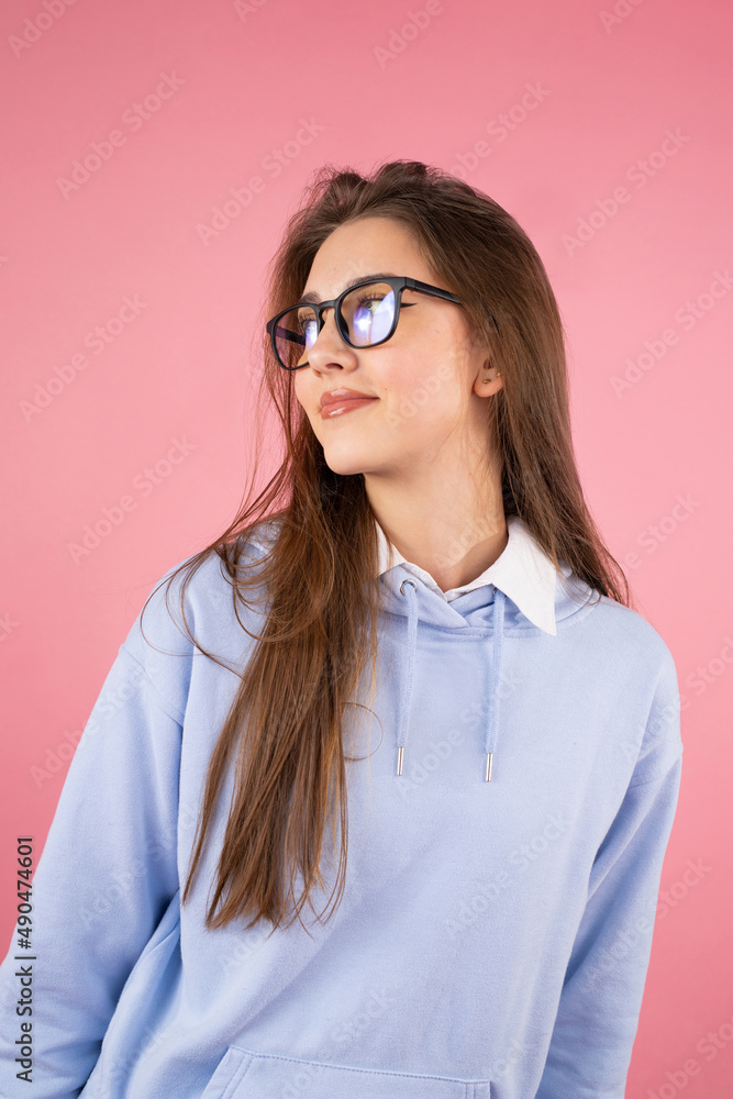 Cheerful young woman college student with blond long hair wearing glasses looking away on isolated pink background.
