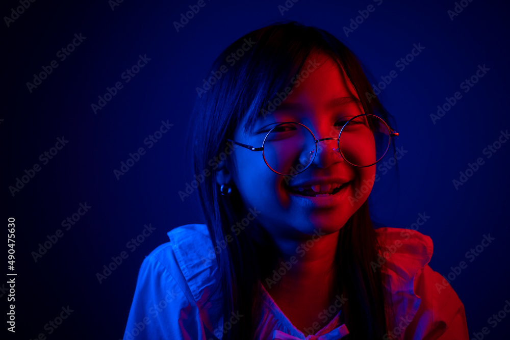 Asian child girl wearing eyeglasses smiling and looking through in the dark with blue and red light Asian child girl wearing eyeglasses smiling and looking through in the dark with blue and red light