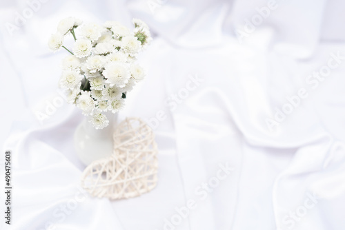 White flowers in white vase on white background with copy space. Top view with selective focus. Greeting or invitation card