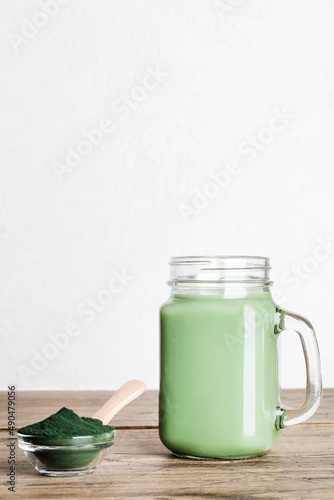 fresh green smoothie in glass bottle and spirulina powder with spoon on wooden background. useful habits  self care and healthy lifestyle. copy space