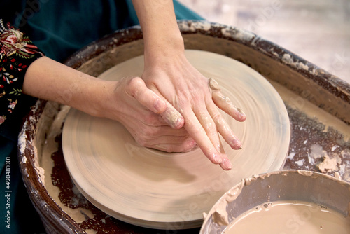 Dirty hands of a ceramist make a cup of clay on a potter's wheel.