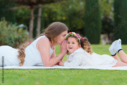 Mother tenderly whispers in the ear of her happy daughter outdoors