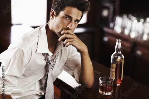 Professional at work, sophisticated after it - Modern Living. A handsome young man winding down after work with a drink at the bar. photo