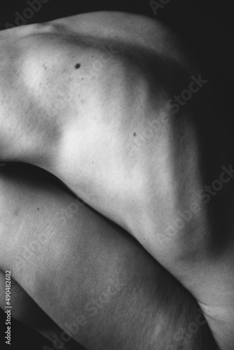 Body details close-up, nude female body. Nude skin photography in black and white. Light defocus and art noise on the frames.Silhouette of a woman's bare back