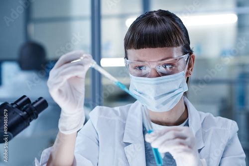 Young woman in mask pouring the blue liquid in test tube during medical researching in laboratory