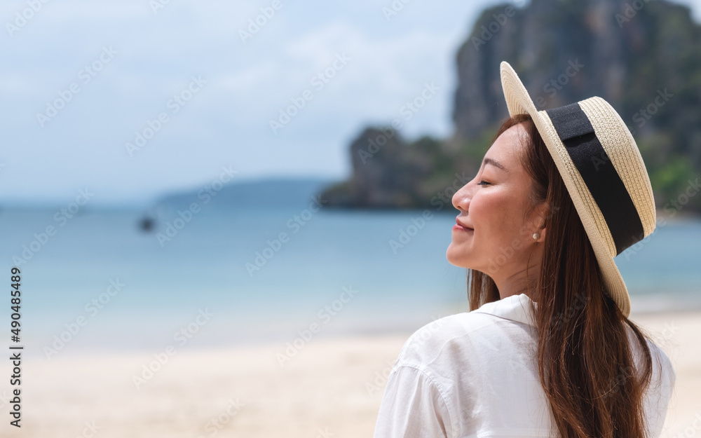 Portrait image of a beautiful young asian woman close her eyes while strolling on the beach with the sea and blue sky background