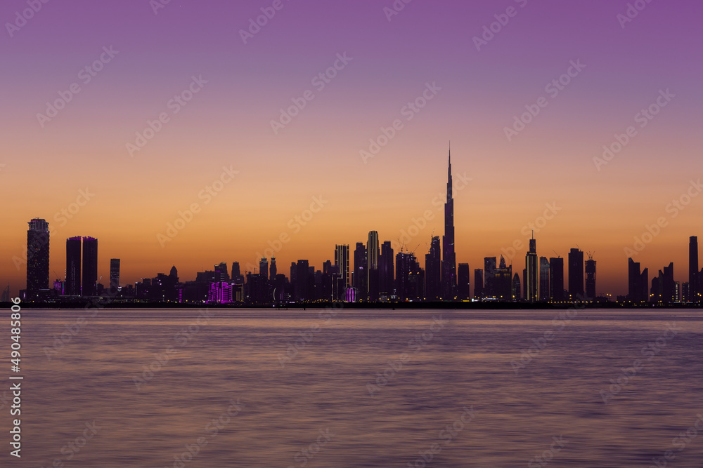 Skyline of Dubai Downtown after sunset during golden hour with purple sky and Dubai Creek Canal, long exposure.