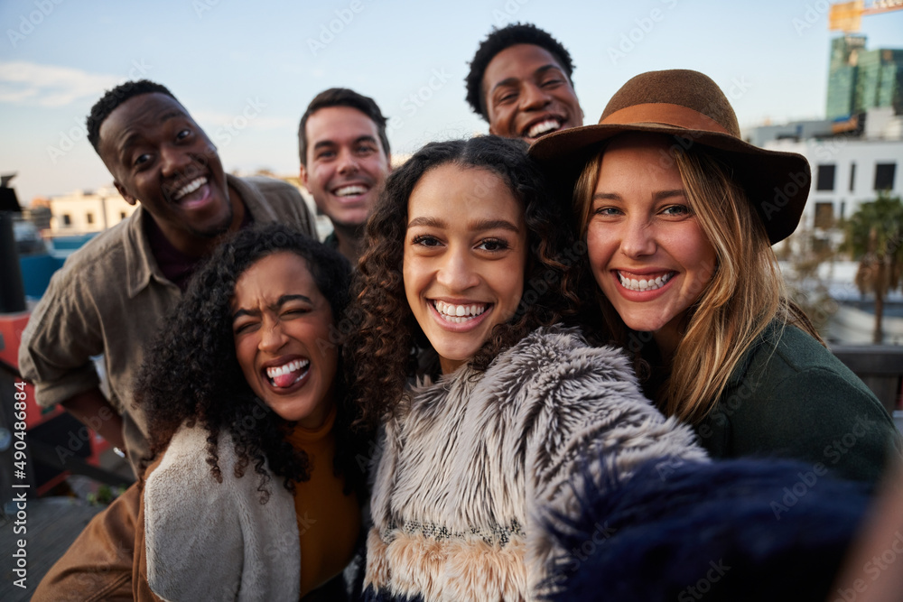 Multi-cultural group of friends taking a selfie at a rooftop party. Smiling and posing at camera in the city. Multi-cultural group of friends taking a selfie at a rooftop party. Smiling and posing at camera in the city.