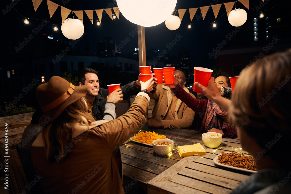 © StratfordProductions - Group of diverse friends sitting, making a toast at an outdoor party around a boho themed table. Red cups and laughs
