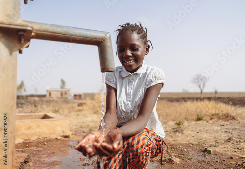 Gorgeous young black African village girl smiling happily at the clean water flowing out of the faucet; water scarsity concept photo