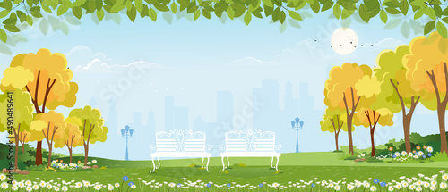 Spring landscape at city park in the morning, Natural public park with flowers blooming in the garden, Peaceful scene of green fields with blurry cityscape building, cloudy and sun on summer