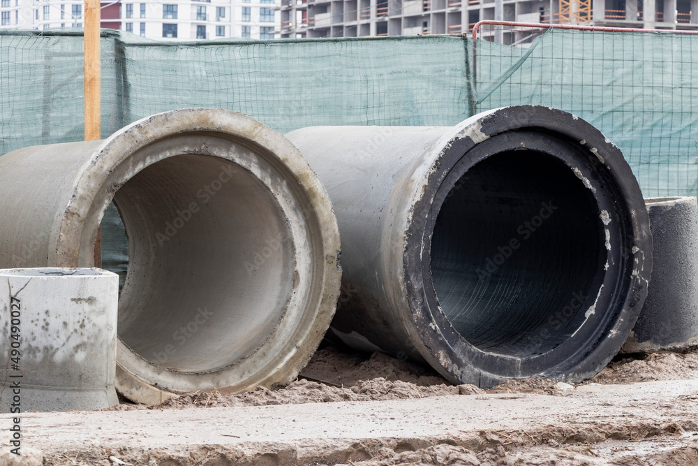 Reinforced concrete storm sewer pipes stacked at a construction site. Large diameter pipes. Sewerage and water supply in a modern city. Reinforced concrete storm sewer pipes stacked at a construction site. Large diameter pipes. Sewerage and water supply in a modern city.