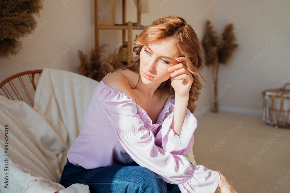 Portrait of a fashionable young woman sitting in a wicker chair in the sun in a room. Portrait of a fashionable young woman sitting in a wicker chair in the sun in a room.