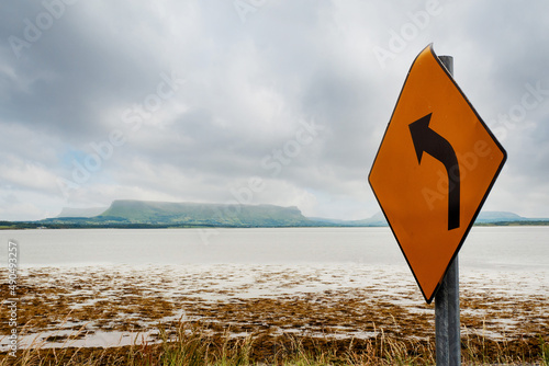 Road sign with arrow pointing in direction of Benbulben flat top mountain in county Sligo, Ireland. Cloudy sky. Famous Irish landmark photo