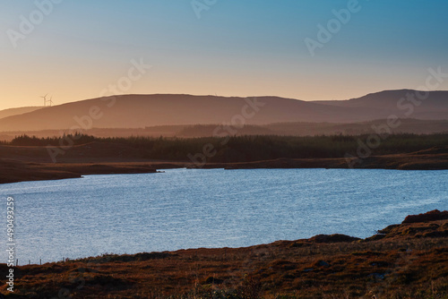 Small lake with blue water and wild fields. Beautiful sun rise scene in Connemara  county Galway  Ireland. Warm and cool tones. Haze over mountains in the background.