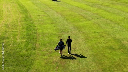Back view of golfer and caddie walking on green field, Hills Golf Club in Molndal near Gothenburg, Sweden. Aerial forward