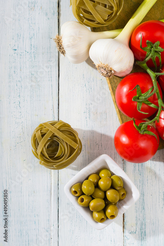 fresh tomato, garlic, olive, uncooked tagliatelle pasta on white wooden table, top view