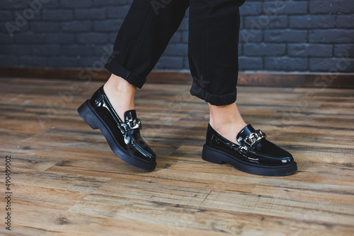 Close-up female legs in black trousers and leather black shoes. Women's shoes in patent leather with a metal buckle. New spring-summer collection of women's leather shoes 2022