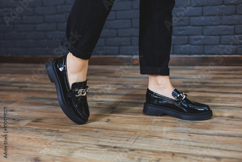 Close-up female legs in black trousers and leather black shoes. Women's shoes in patent leather with a metal buckle. New spring-summer collection of women's leather shoes 2022 photo