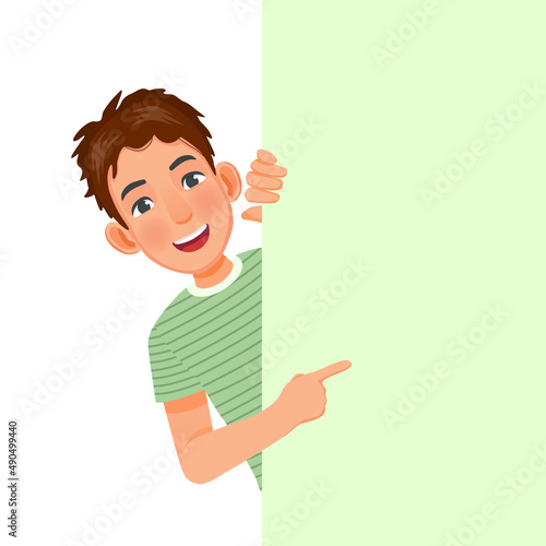 handsome young man peeking from behind blank billboard pointing index finger to empty banner for copyspace advertising and announcement messages