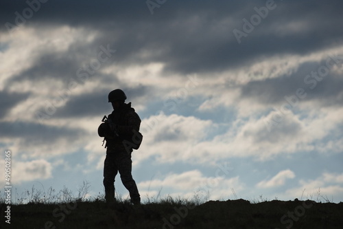 Silhouette of a soldier with a machine gun on the background of the sky with clouds