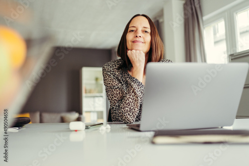 satisfied business woman with laptop rests her chin on her hand