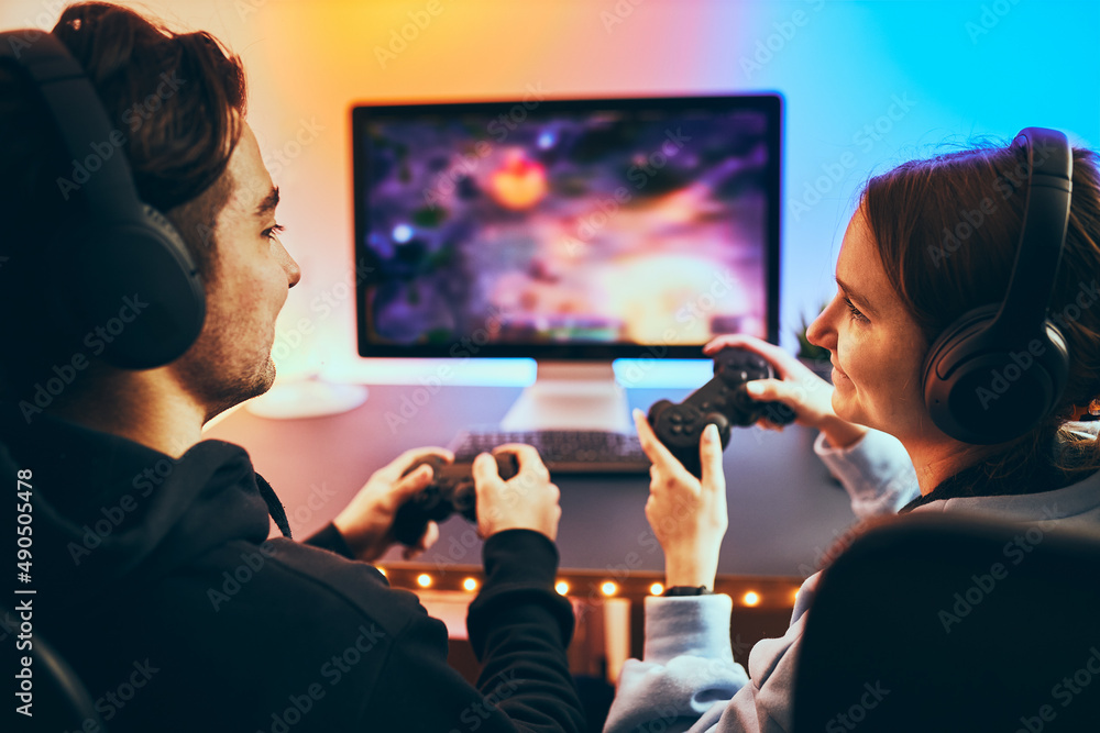 Friends playing video game at home. Gamers playing online in dark room lit  by neon lights. Competition and having fun - a Royalty Free Stock Photo  from Photocase