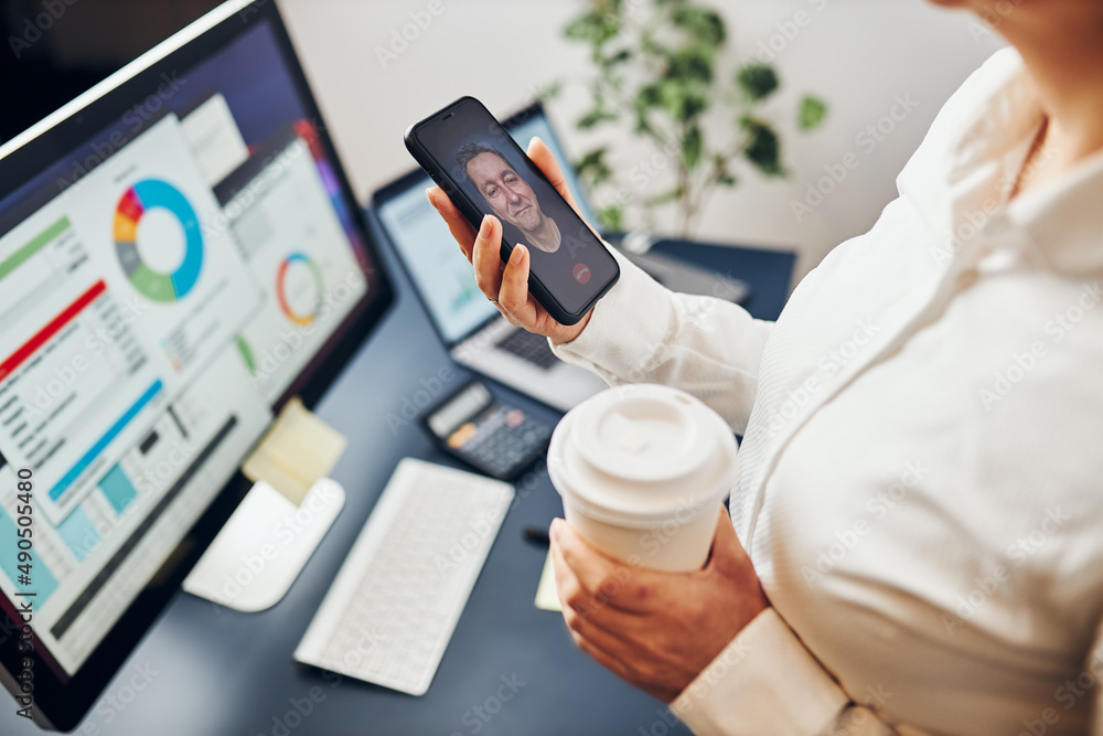 Businesswoman having video chat on mobile phone with her colleague. Businesswoman working with data on charts, graphs and diagrams on computer screen Businesswoman having video chat on mobile phone with her colleague. Businesswoman working with data on charts, graphs and diagrams on computer screen