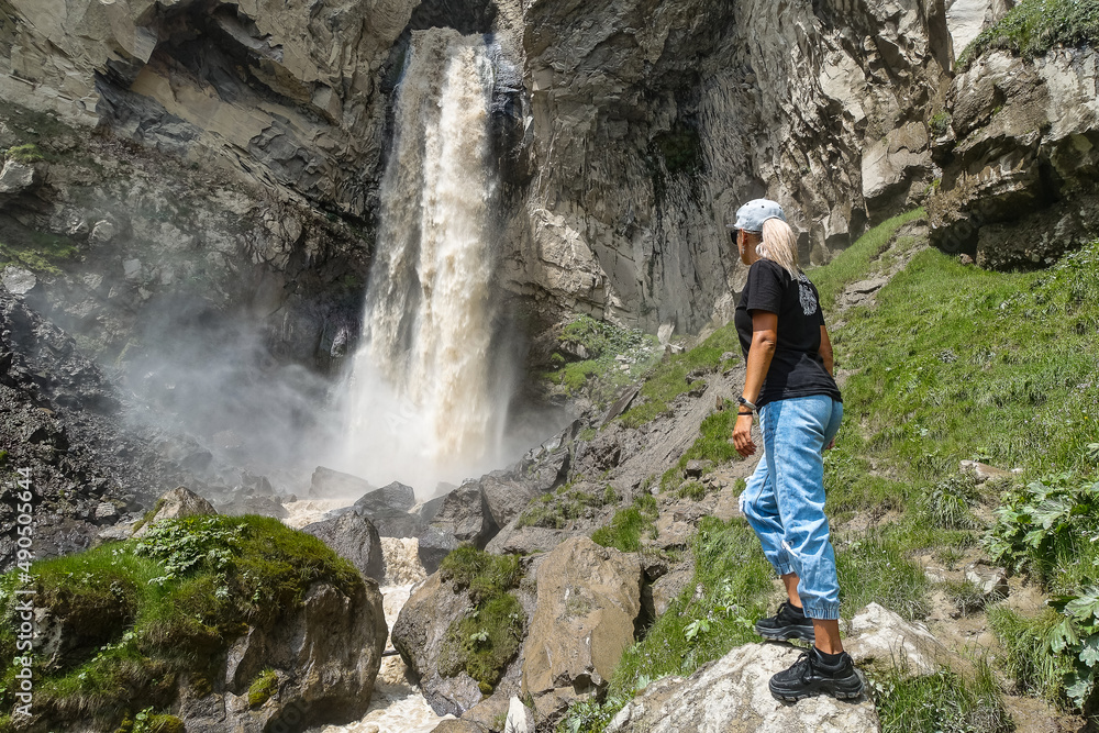 Obraz premium A girl at the Sultan-su waterfall surrounded by the Caucasus Mountains near Elbrus, Jily-su, Russia