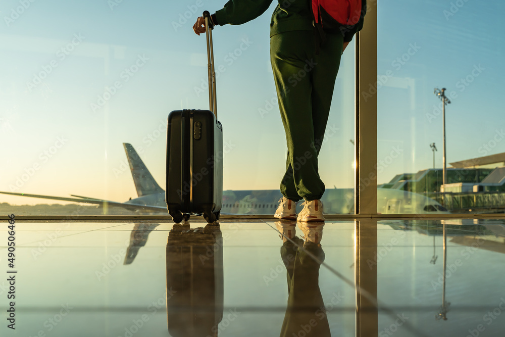 woman with carry-on suitcase looking through the windows of the airport.