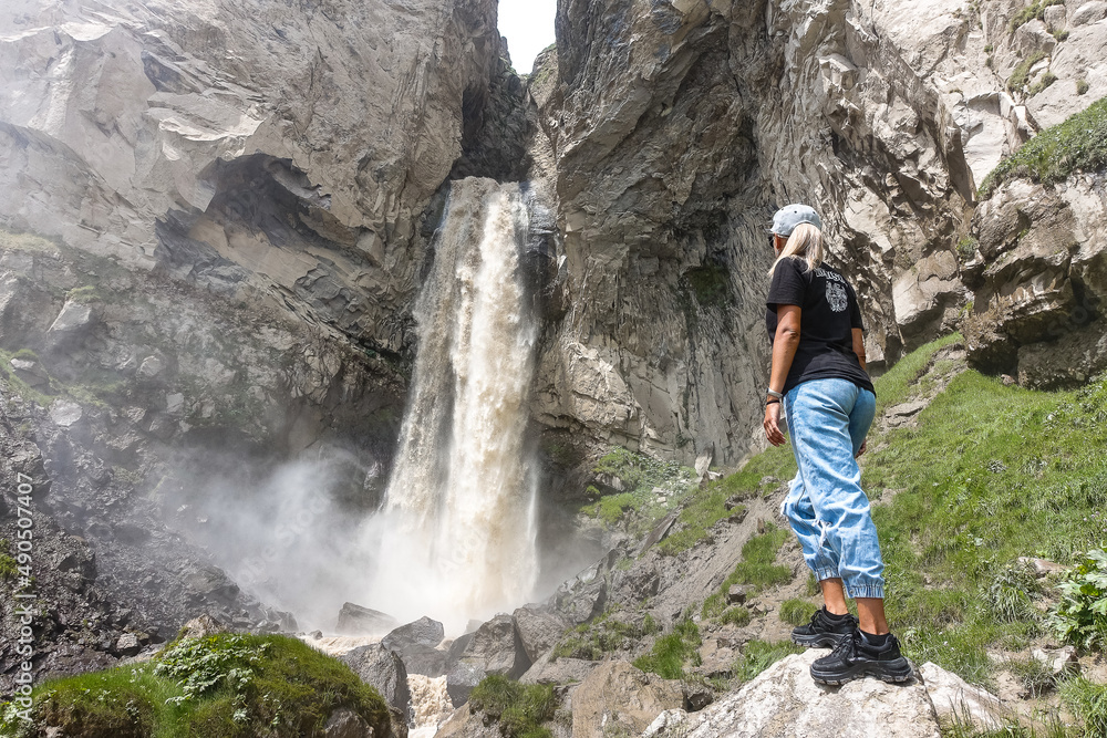 A girl at the Sultan-su waterfall surrounded by the Caucasus Mountains near Elbrus, Jily-su, Russia