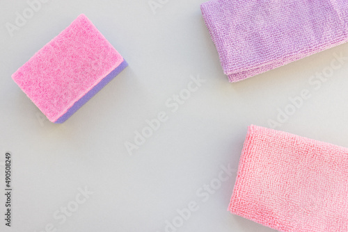 Pink and purple sponge and microfiber cloth for cleaning and dusting on gray background. Accessories for cleaning kitchen and home concept. Top view, copy space