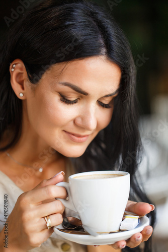 Portrait of pretty young business woman with cup in hands. Caucasian modern girl is drinking coffee in the morning in city cafe. Close up face portrait