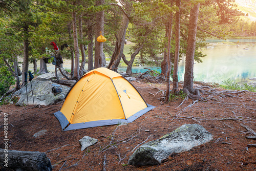 A lonely orange tent is set up in the forest near the lake. Weekend activity and hiking or trekking adventures