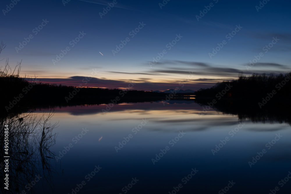 Landscape with water reflection and fading light at twilight - silhouette of forest on shore