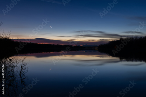 Landscape with water reflection and fading light at twilight - silhouette of forest on shore