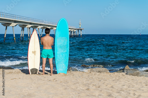 handsome man stand with surfing board at surf spot at sea ocean beach and wait for wave. View from back.