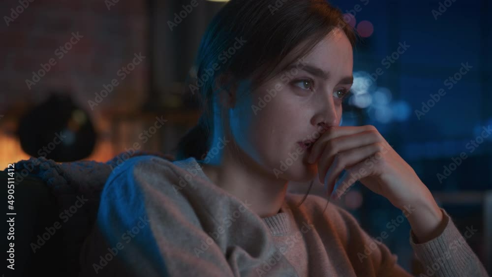 Portrait of Pretty Female Spending Time at Home, Resting on a Sofa, Watching Horror TV Show in Stylish Loft Apartment. Young Woman Enjoy Watching Scary Movie Alone on Streaming Service. Portrait of Pretty Female Spending Time at Home, Resting on a Sofa, Watching Horror TV Show in Stylish Loft Apartment. Young Woman Enjoy Watching Scary Movie Alone on Streaming Service.