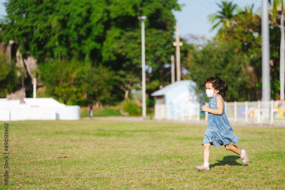 Portrait cute kid girl running on green grass. Child wearing face mask prevent virus and air pollution PM2.5. Children playing sport in summer time. Hot weather. Empty space for enter text. Portrait cute kid girl running on green grass. Child wearing face mask prevent virus and air pollution PM2.5. Children playing sport in summer time. Hot weather. Empty space for enter text.