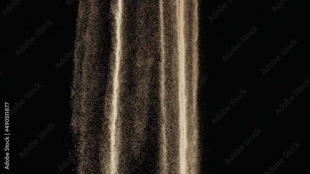 Particles of white dry sand are pouring down on black studio background. Close up shot stream of flowing natural sand grains. The sand flows down. Slow motion.