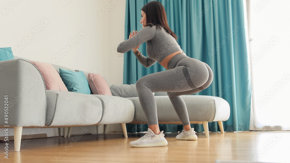 Fototapeta premium female butt workout squats at home. Athletic Woman squats workout in living room. Female gymnastics. Glutes workout motivation. Fitness at home concept.