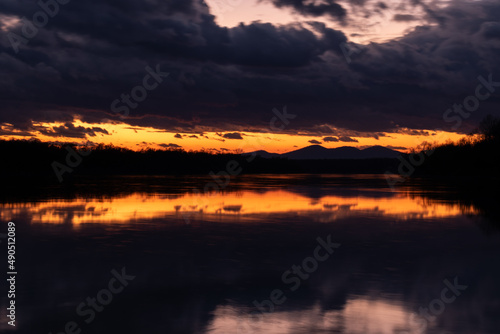 Twilight landscape with dark ominous storm clouds and fading orange glow at sky above horizon - symmetric reflection © slobodan
