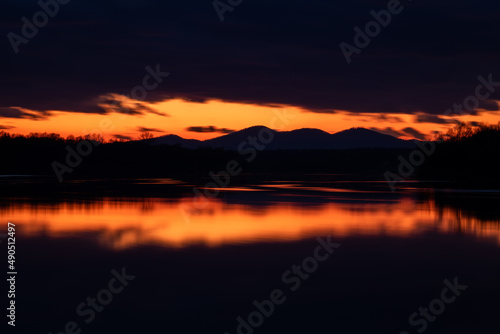 Last light in sky above mountain silhouette framed with dark clouds at twilight - landscape with symmetric reflection on water surface