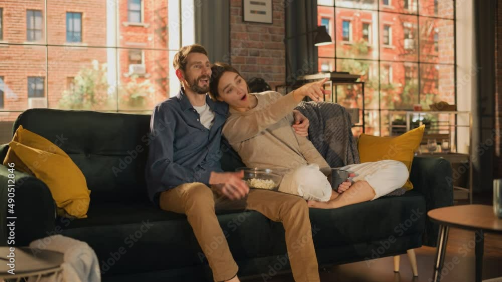 Portrait of Young Couple Spending Time at Home, Sitting on a Sofa, Man Embracing His Girlfriend While Watching Exciting TV Show in Apartment. Man and Woman Streaming Movie and Get Surprised. Portrait of Young Couple Spending Time at Home, Sitting on a Sofa, Man Embracing His Girlfriend While Watching Exciting TV Show in Apartment. Man and Woman Streaming Movie and Get Surprised.